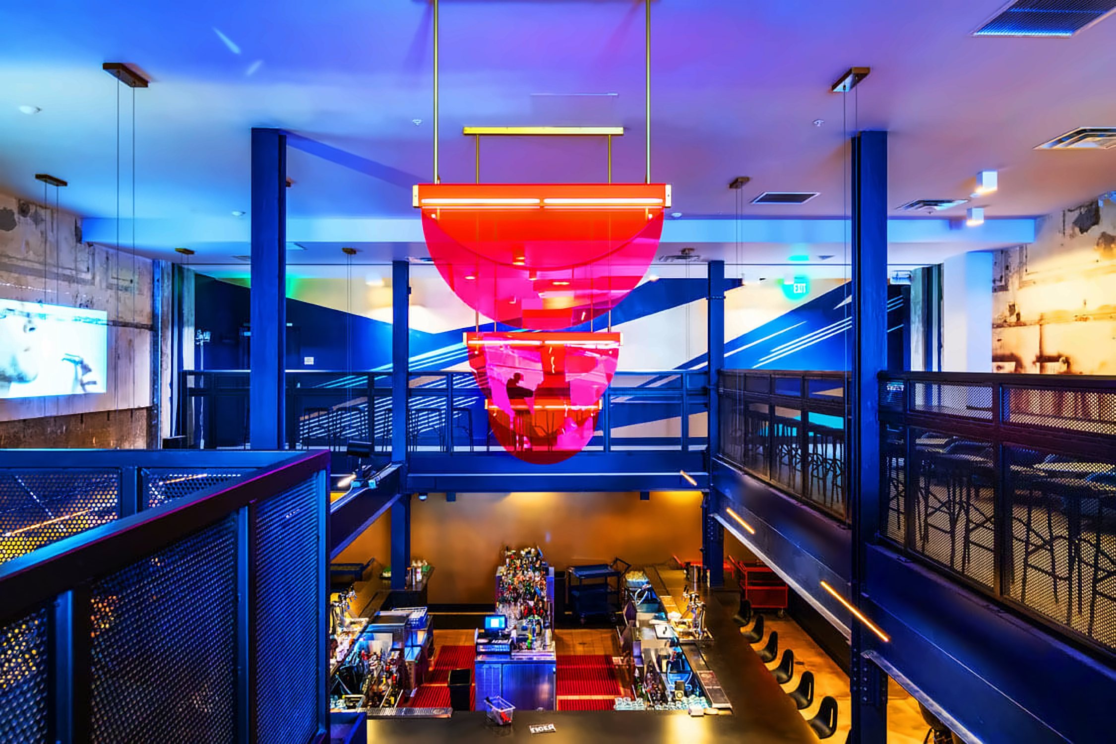 Two-level bar interior with steel framing and a suspended sculpture